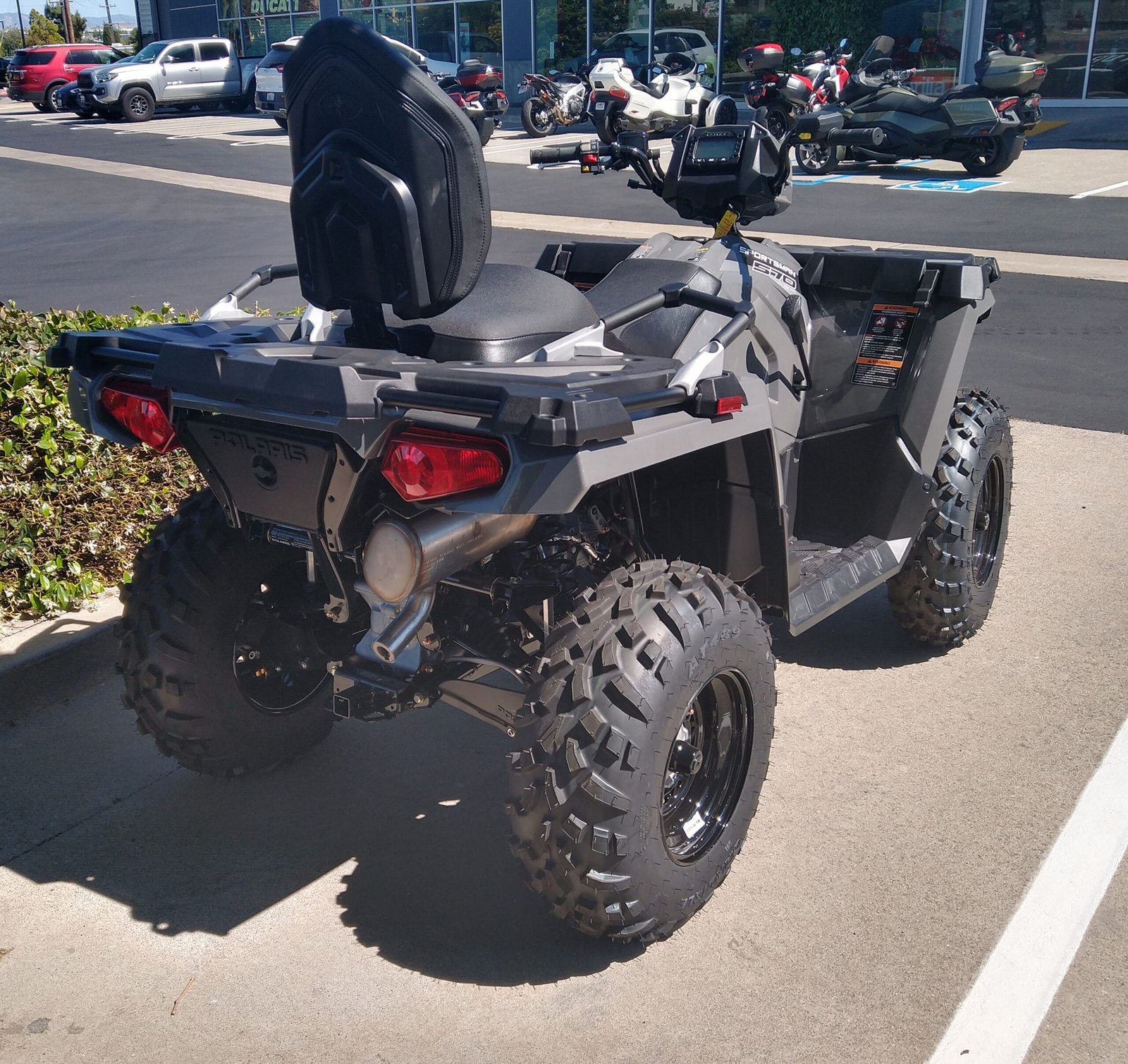 Gray Polaris Sportsman utility quad with passenger backrest and knobby tires, parked on a paved lot